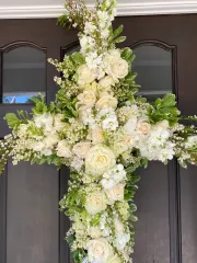 Floral cross made of white roses and greenery, hanging on a brown door.