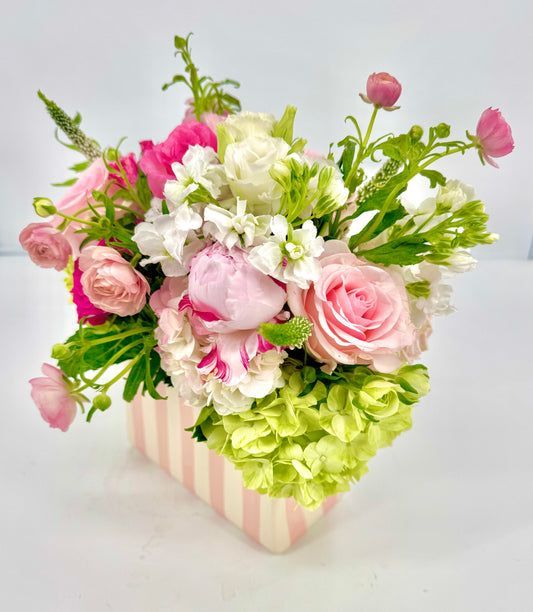Floral arrangement in pink and white striped vase; features roses, peonies, and other blooms.