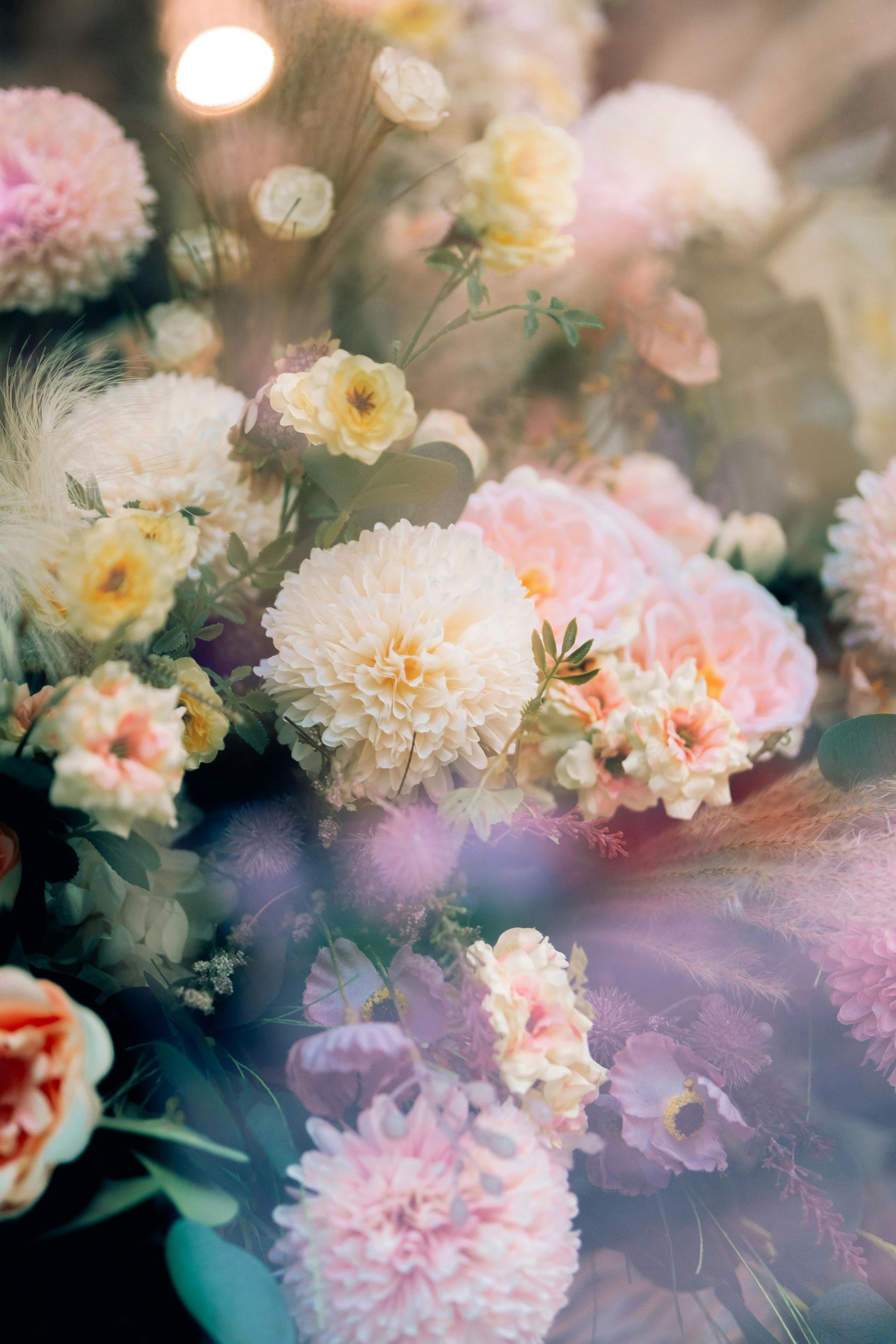 Assortment of pastel-colored flowers, including pink dahlias and yellow roses, create a soft, dreamy arrangement.