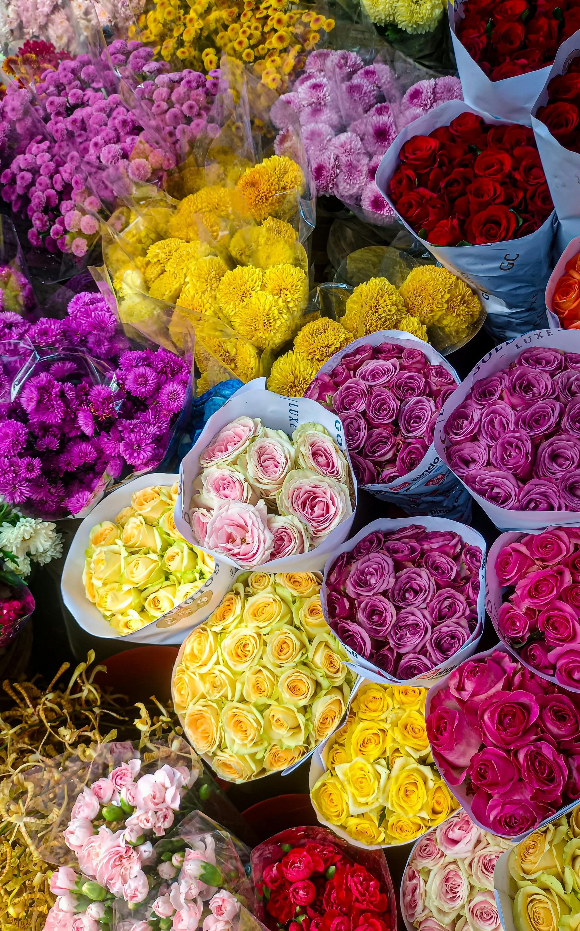 Bundles of colorful flowers for sale, including pink, yellow, red, and purple roses and other blooms.