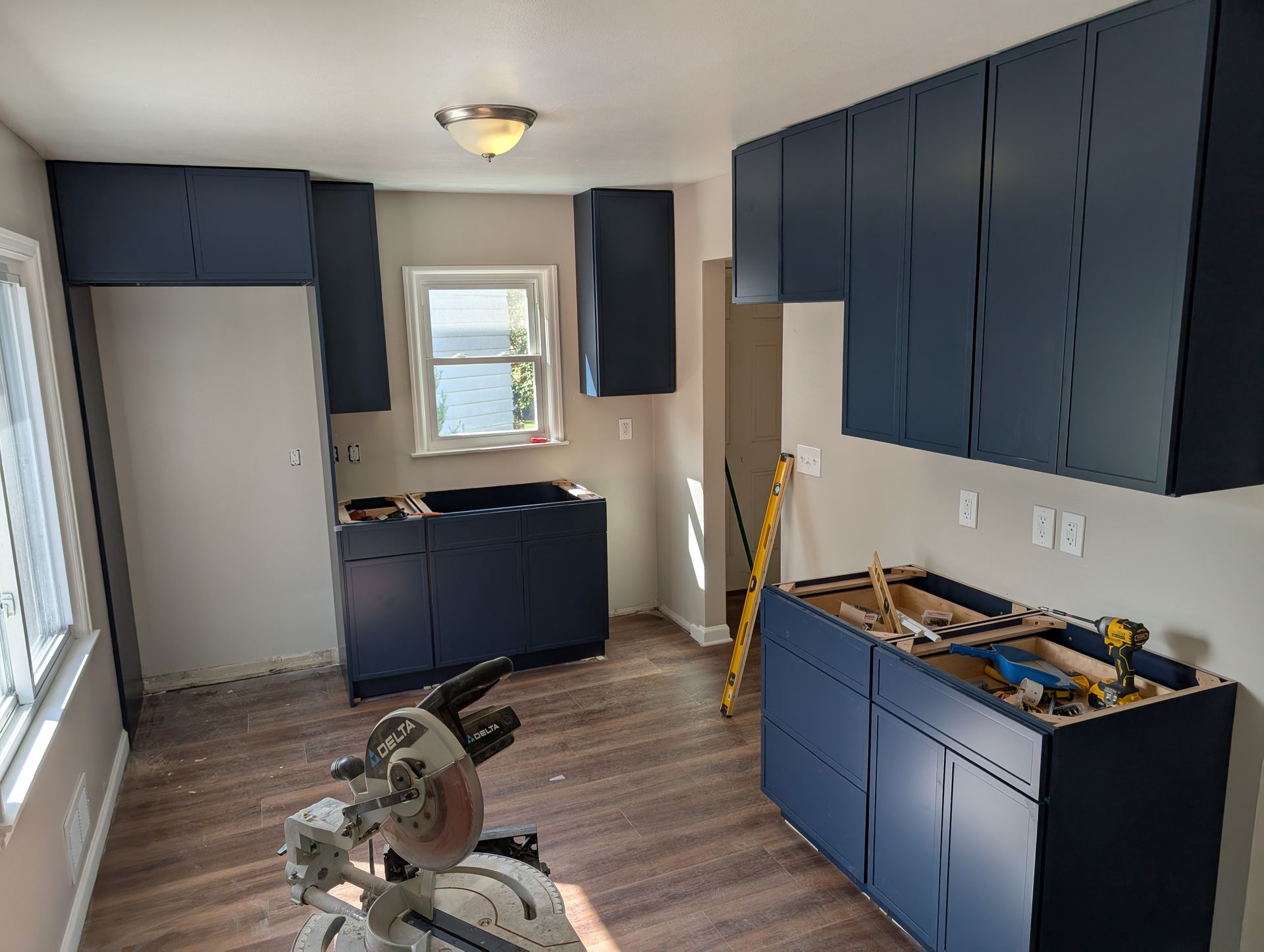 Blue kitchen cabinets in an unfinished room with wood flooring and tools on the floor