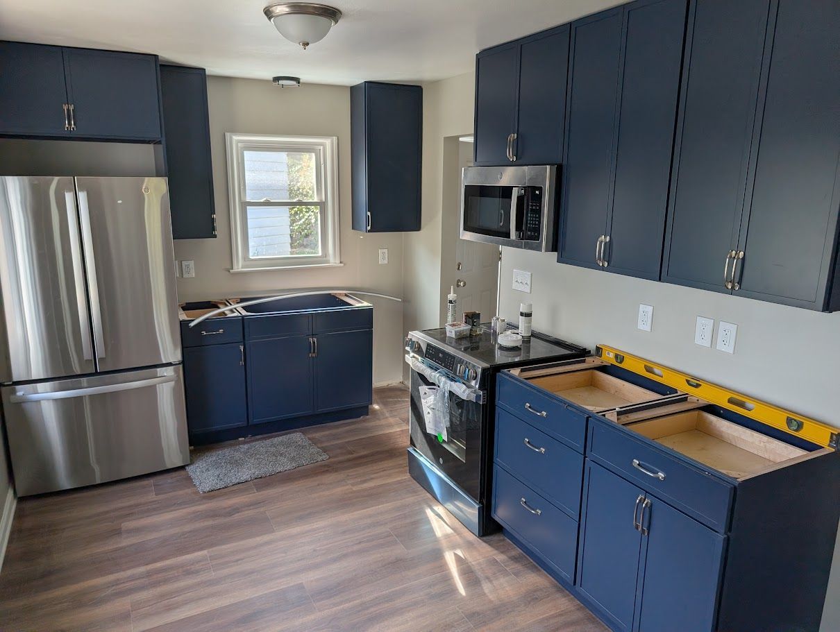 Blue kitchen with stainless steel appliances, window over the sink, and unfinished countertop on the right