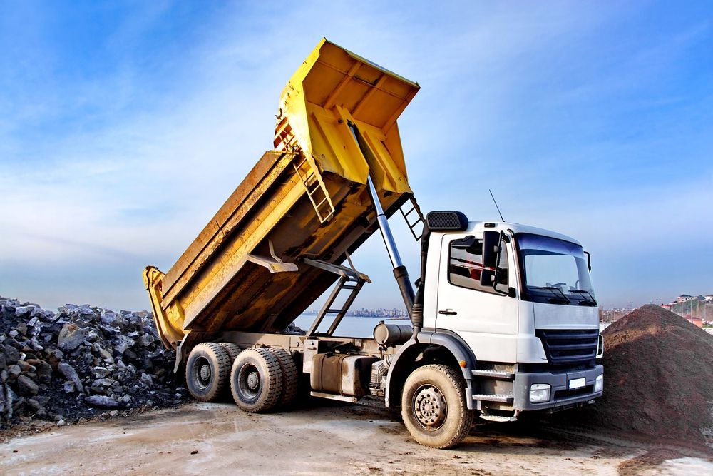 Yellow Dump Truck Unloading Materials at a Construction Site Against a Blue Sky — Des’s Driving School in Ulladulla, NSW