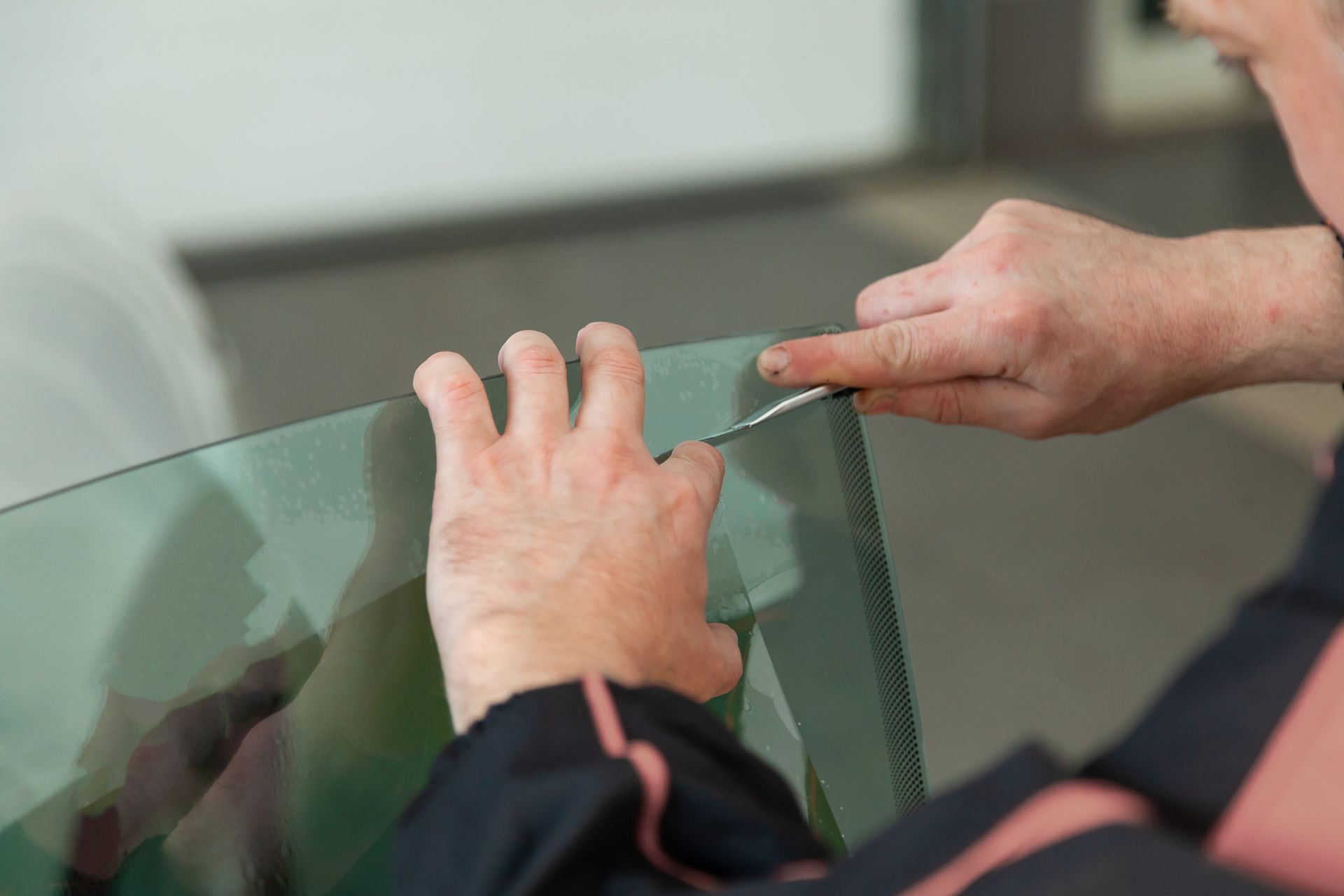 Person trimming window tint film with a blade; hands close-up.