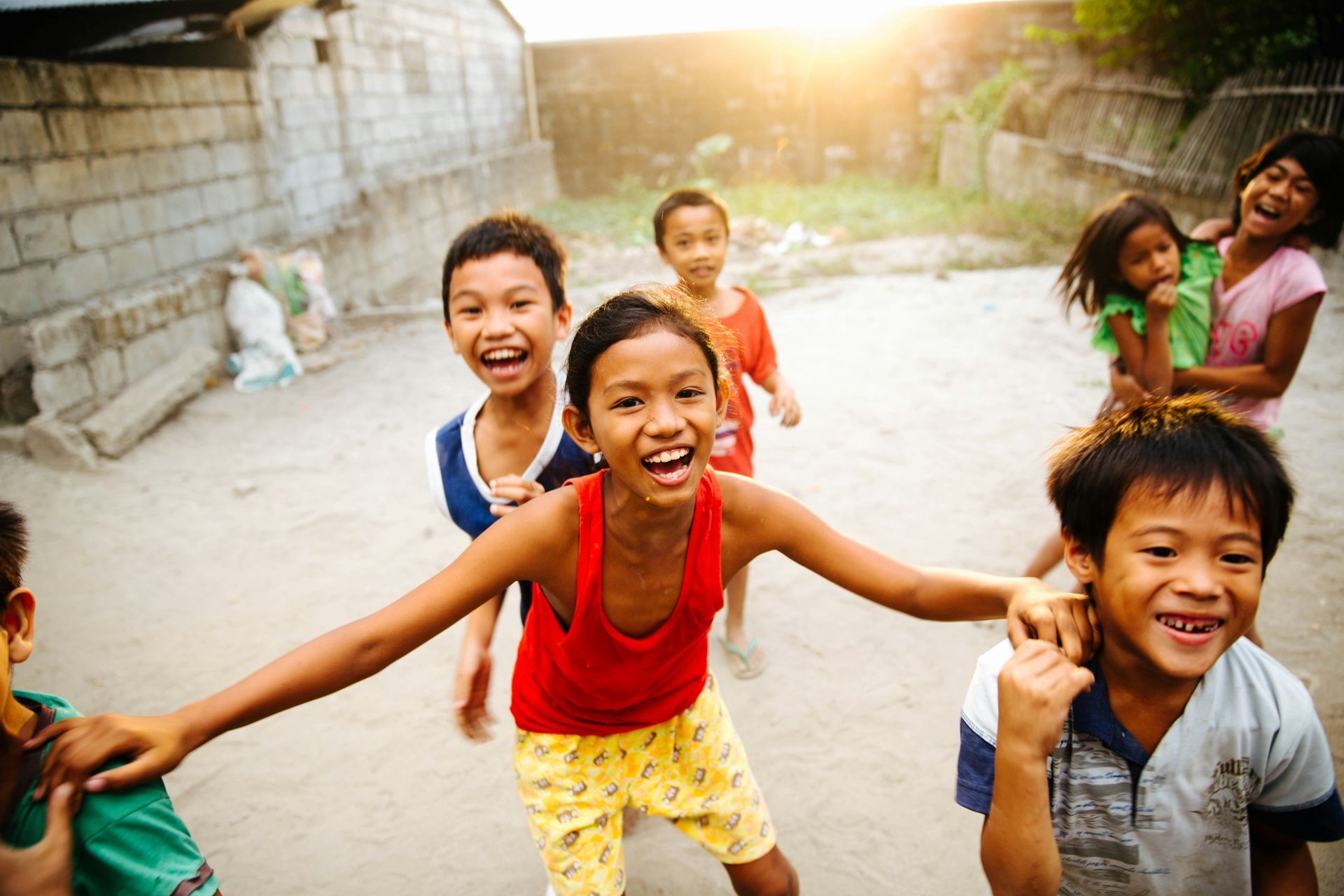 Children smiling and running on a sunlit street, one in a red shirt in the foreground