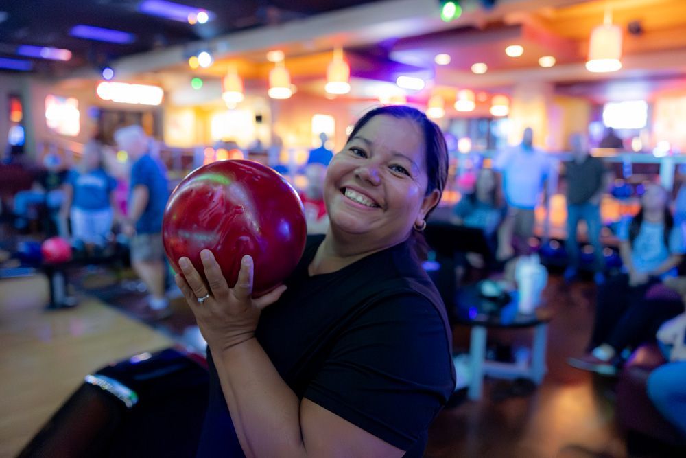 Smiling person holding a red bowling ball in a brightly lit bowling alley
