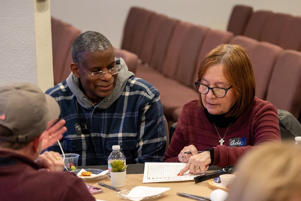 People seated at a table in a meeting, reviewing notes and talking in a conference room.