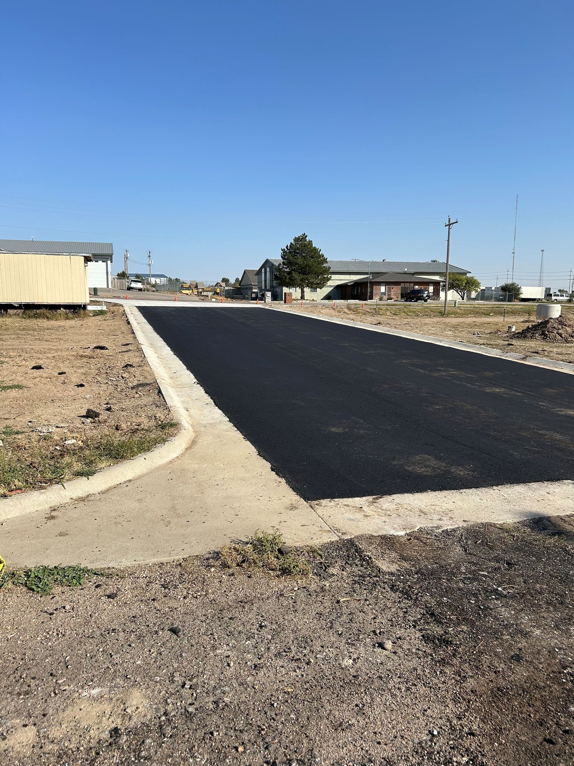 A newly paved road in a residential area with a house in the background.
