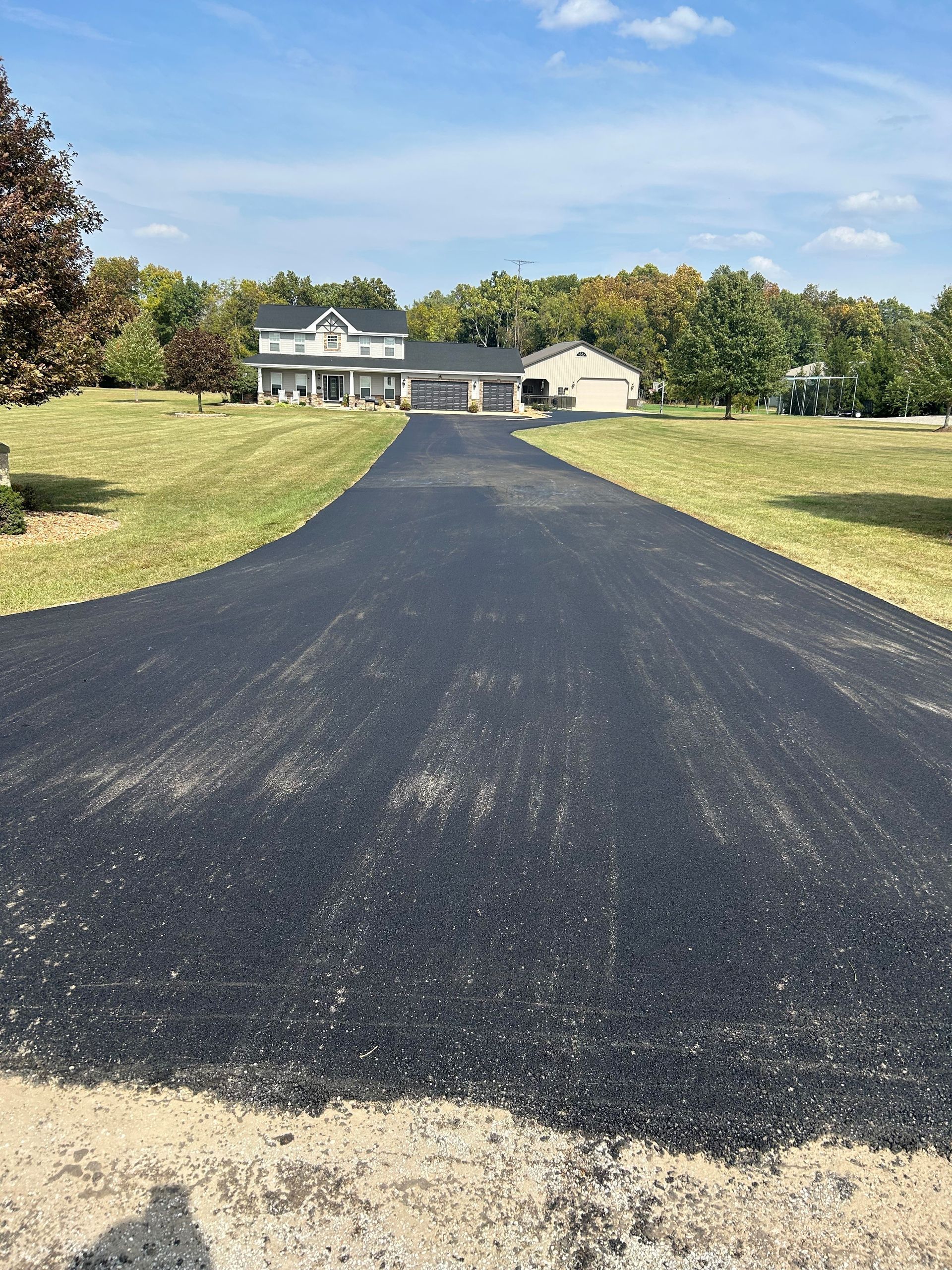 A driveway leading to a house in the middle of a grassy field.