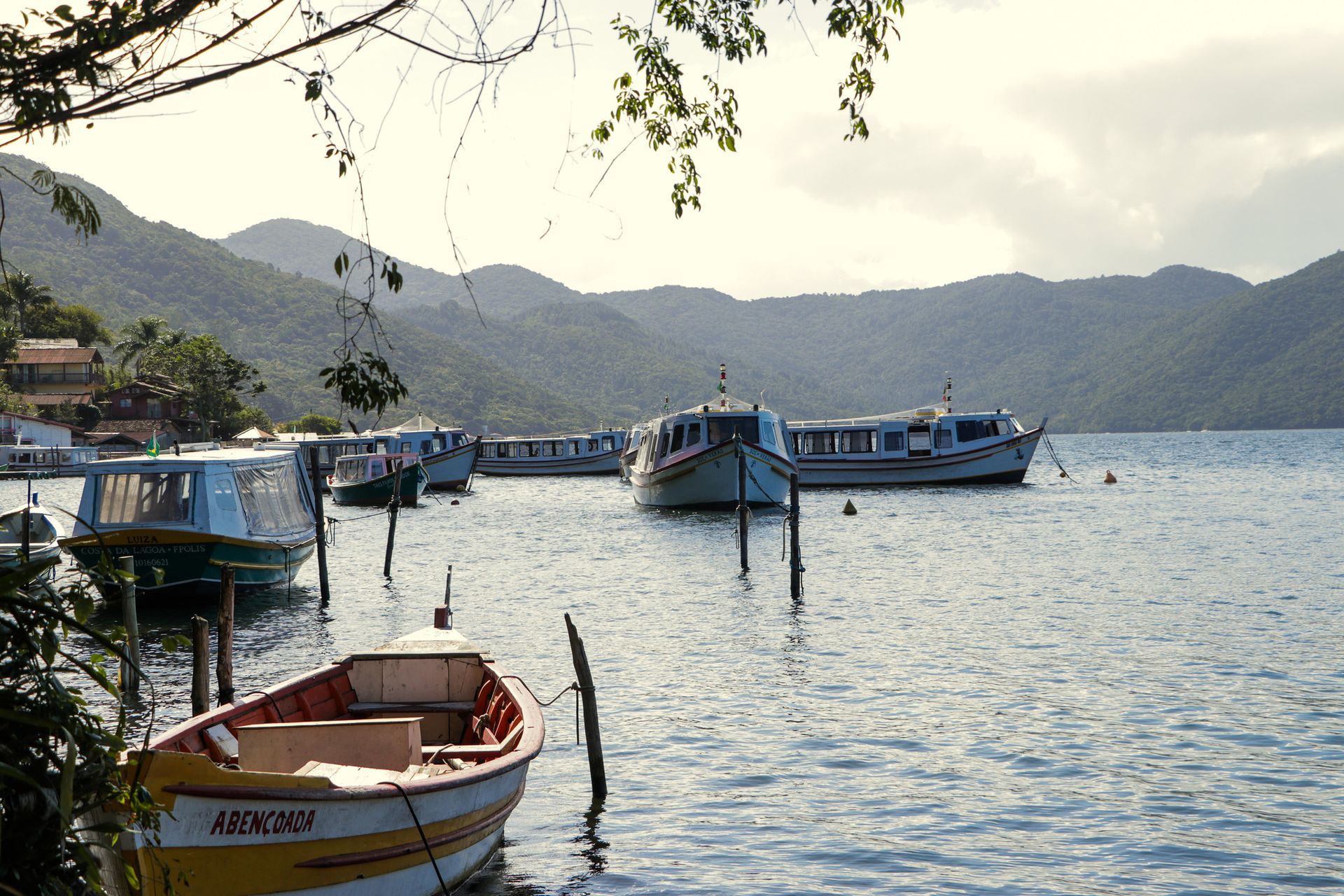 Barcos ancorados em águas calmas, montanhas ao fundo, um dia ensolarado.