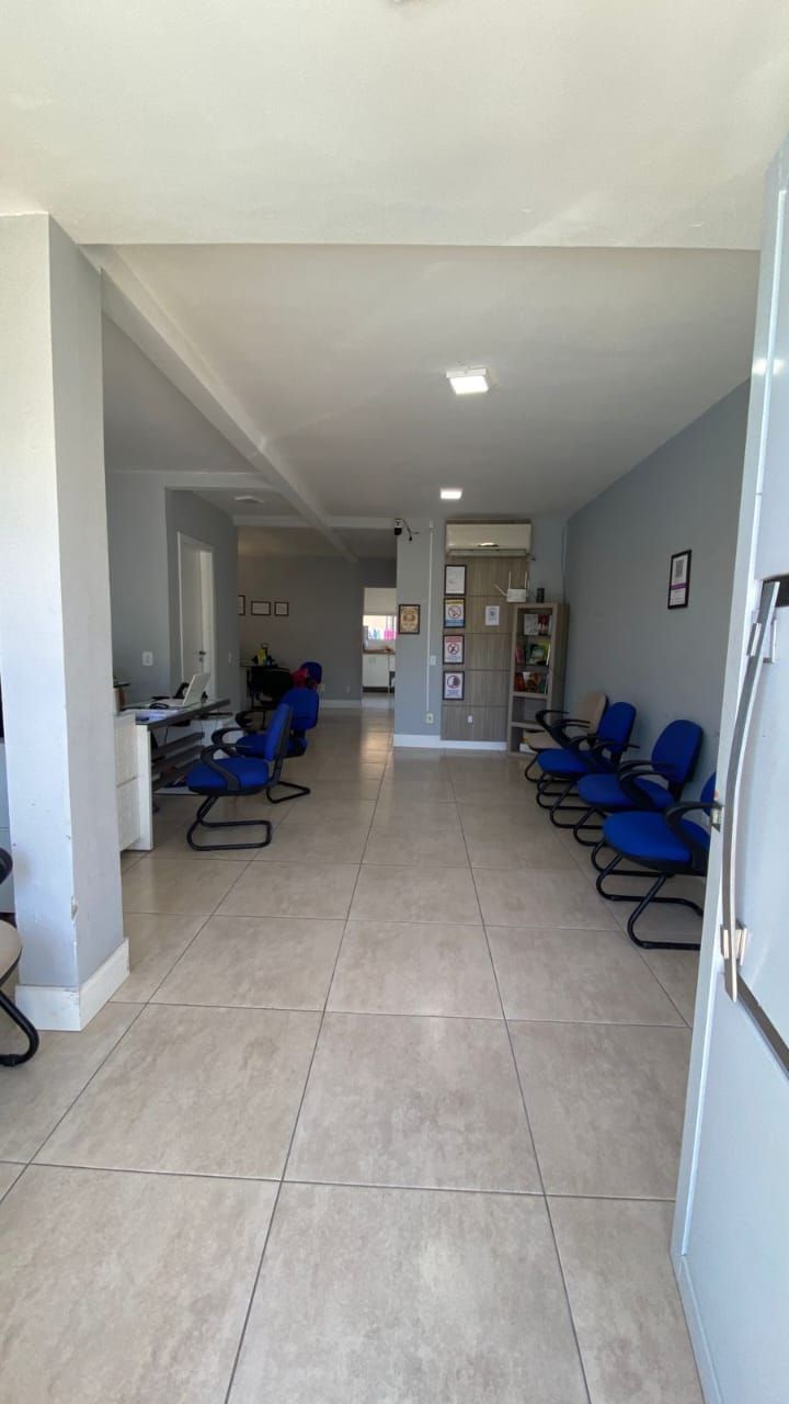 Sala de espera com cadeiras azuis, piso de azulejo claro e paredes cinza.