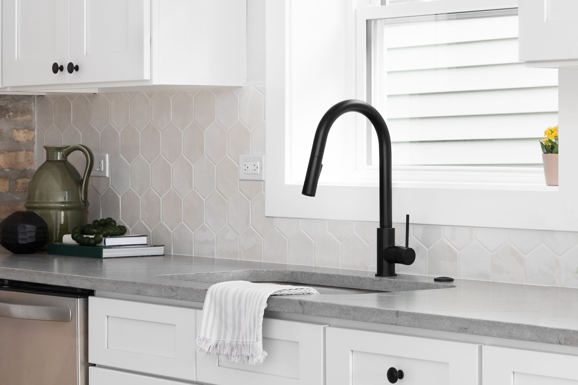 Bright white kitchen with gray countertops, black faucet, and a window above the sink.