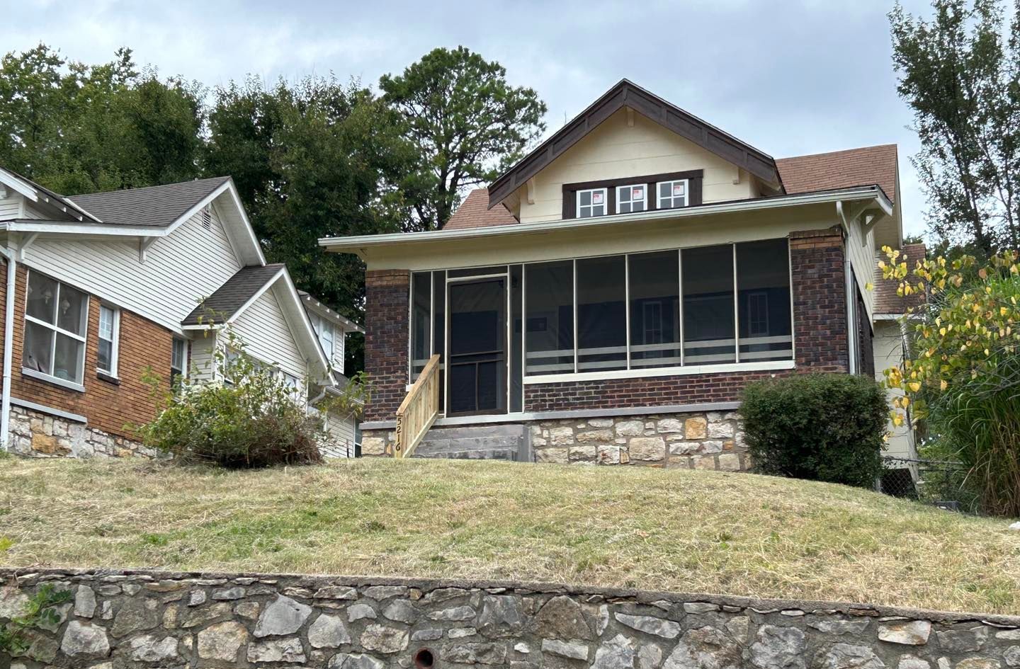 A house with a screened in porch is sitting on top of a hill next to a stone wall.
