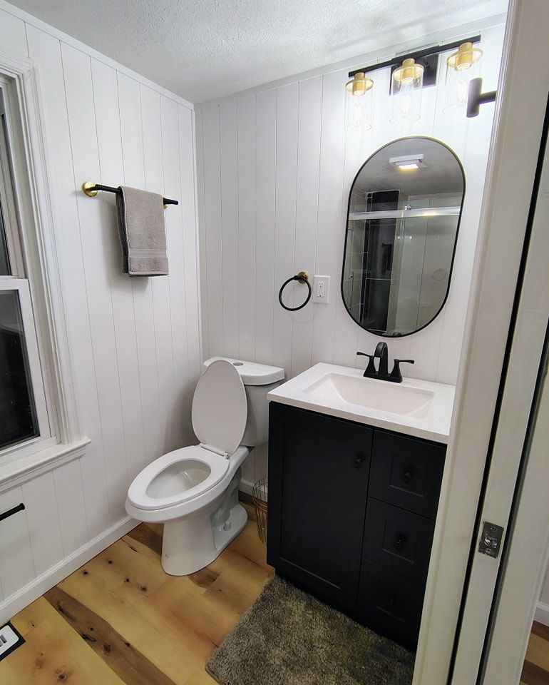 A bathroom with a toilet , sink , mirror and window.