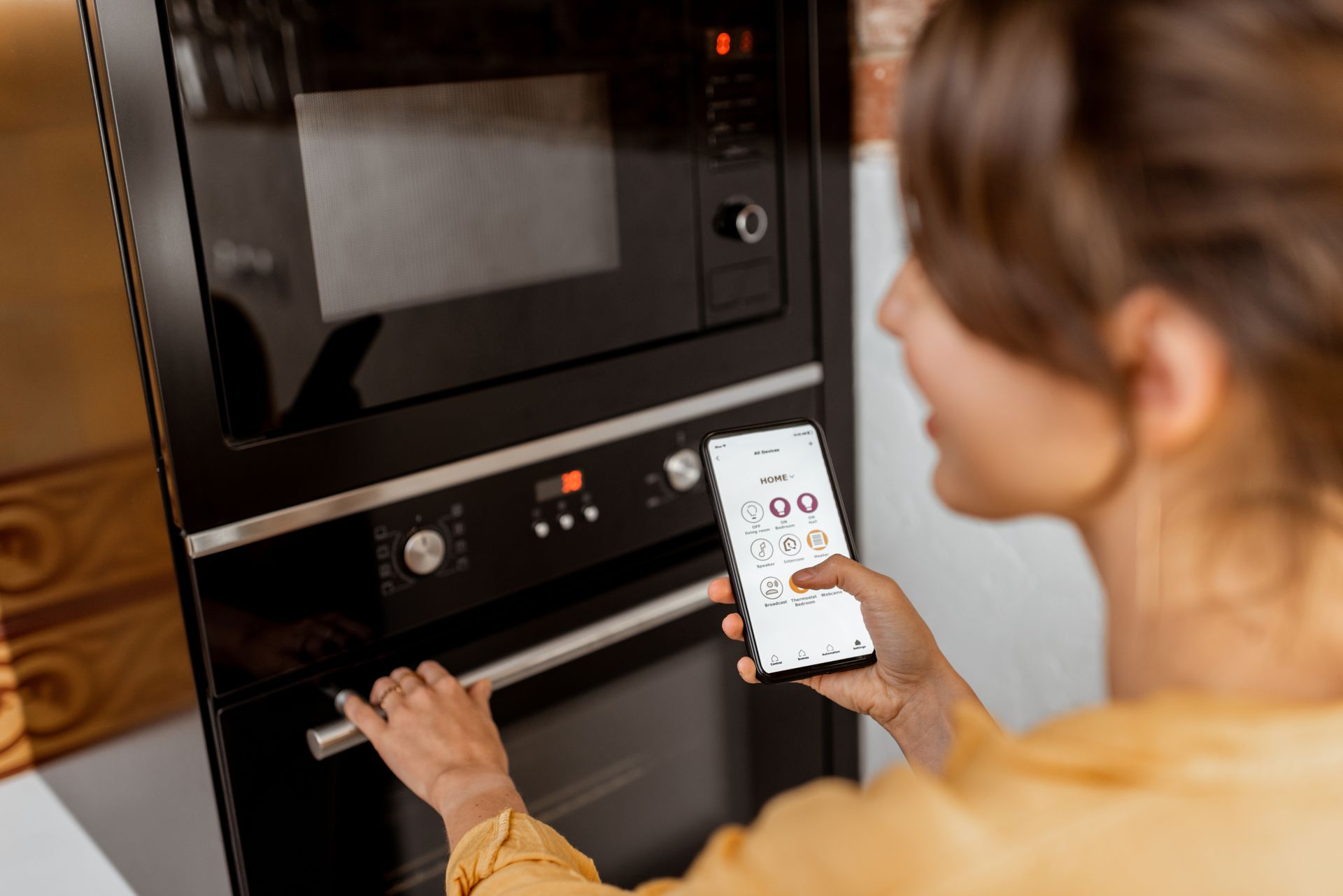 Person using a smartphone to control a black built-in oven in a kitchen