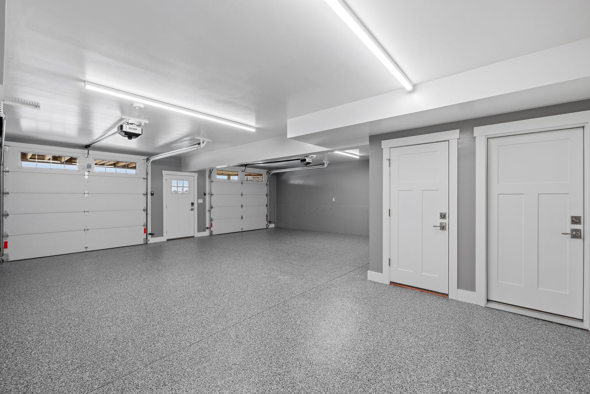 Spacious, modern garage with three garage doors and two white doors on a speckled gray floor.