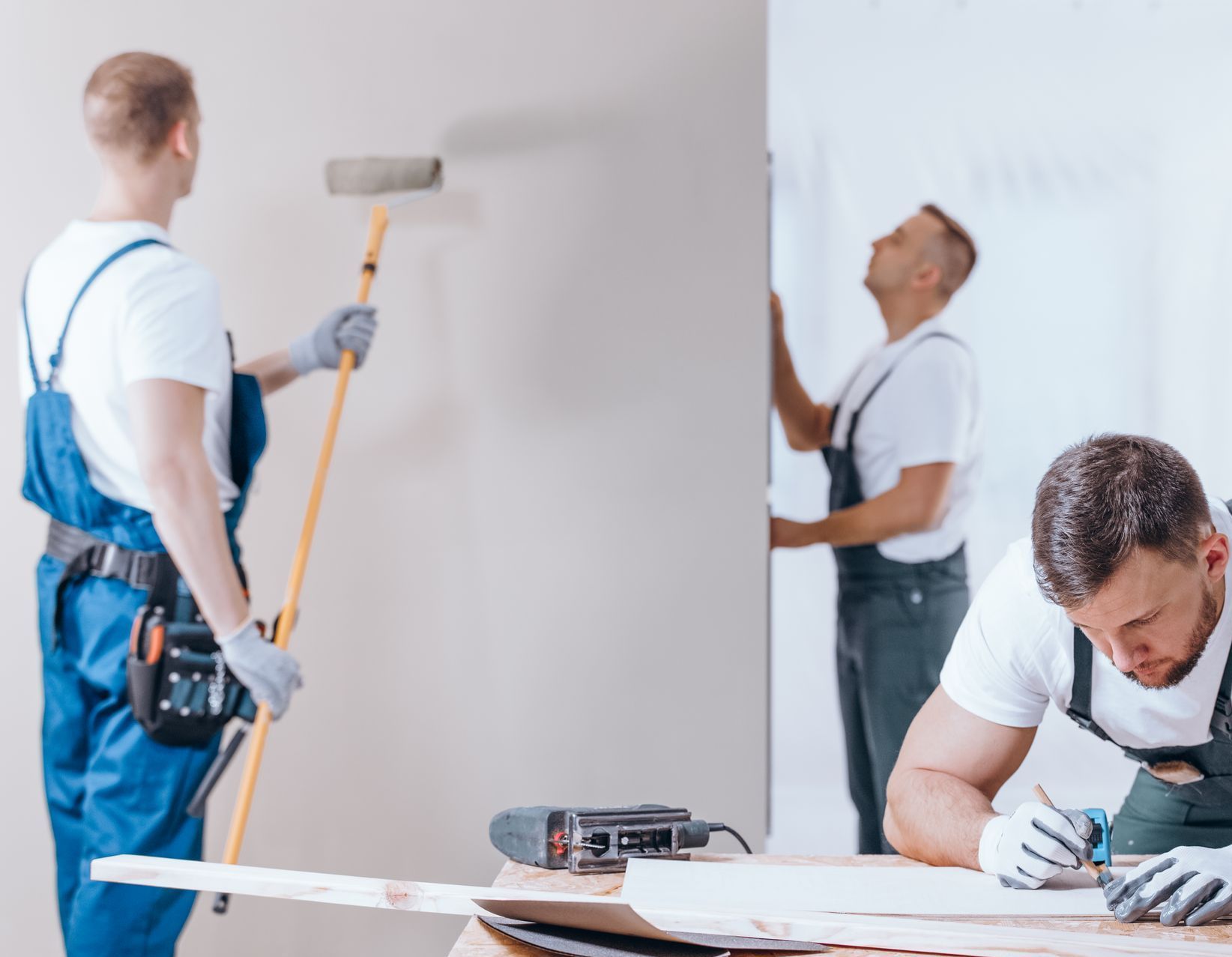 Two men are painting a wall in a room.