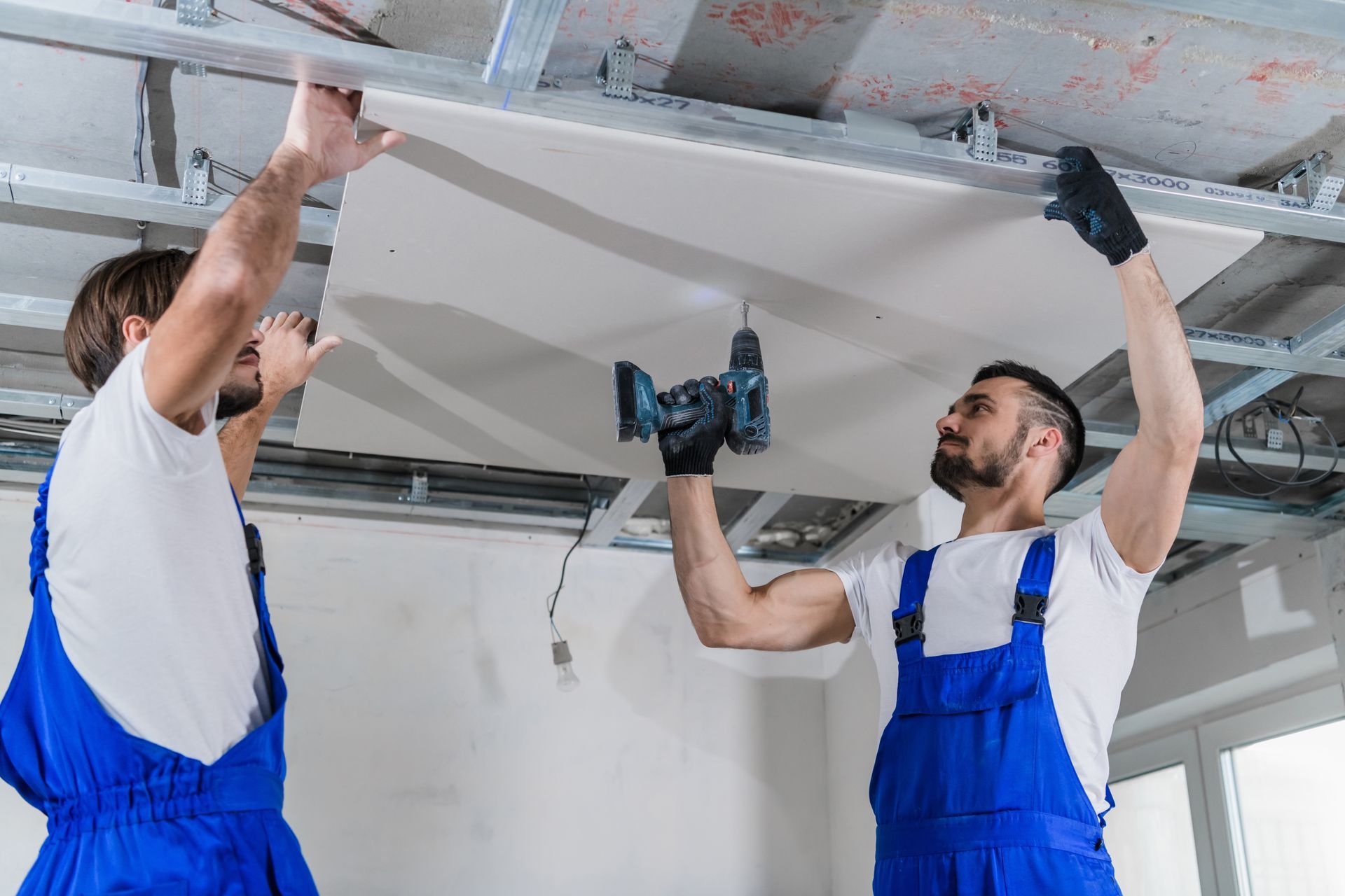 Two men are working on a ceiling with a drill.