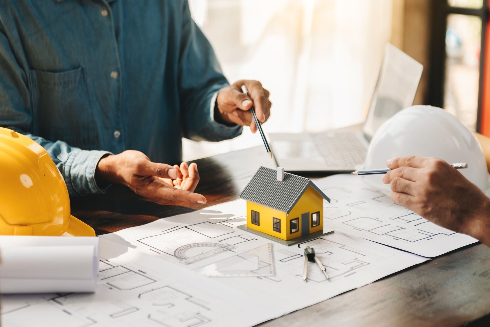Two men are sitting at a table with a model house and blueprints.