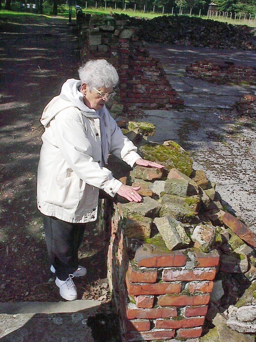 Elderly woman in a white coat touching moss-covered brick ruins in a sunlit park
