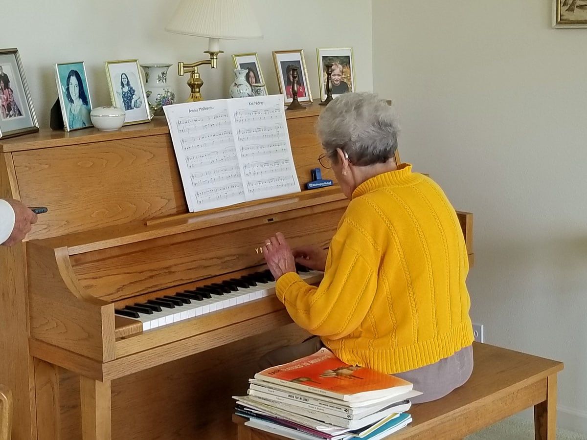 Person in yellow sweater playing an upright piano in a living room with framed photos on top.