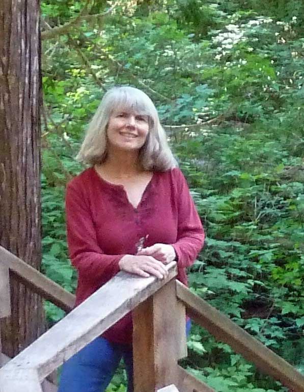 Woman in a red blouse leaning on a wooden railing in a lush green forest.