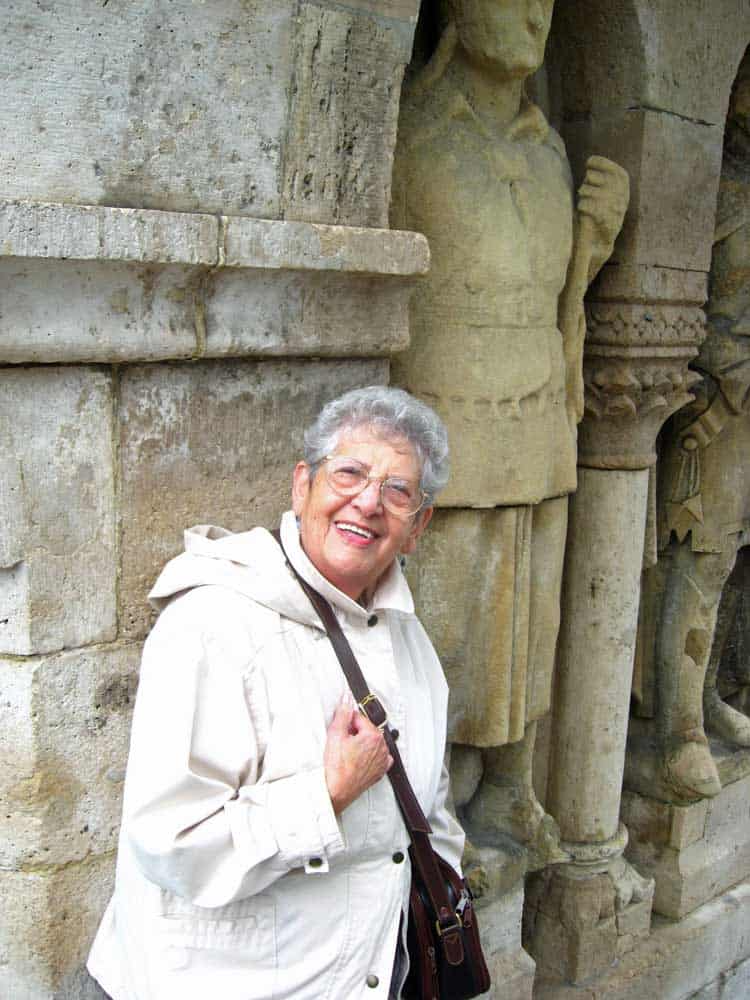 Smiling woman in a white jacket standing beside stone carved figures at an ancient ruin