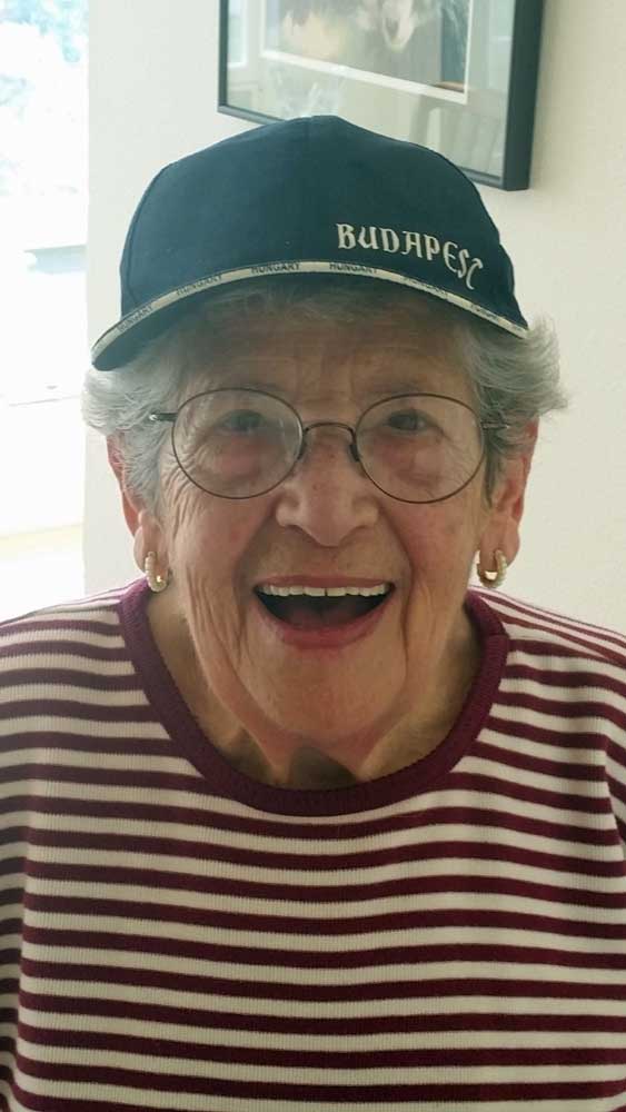 Smiling person wearing a black cap and striped shirt, indoors by a framed picture.