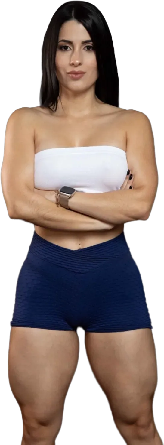 Woman standing against a white background with arms crossed, wearing a white tube top and blue shorts.