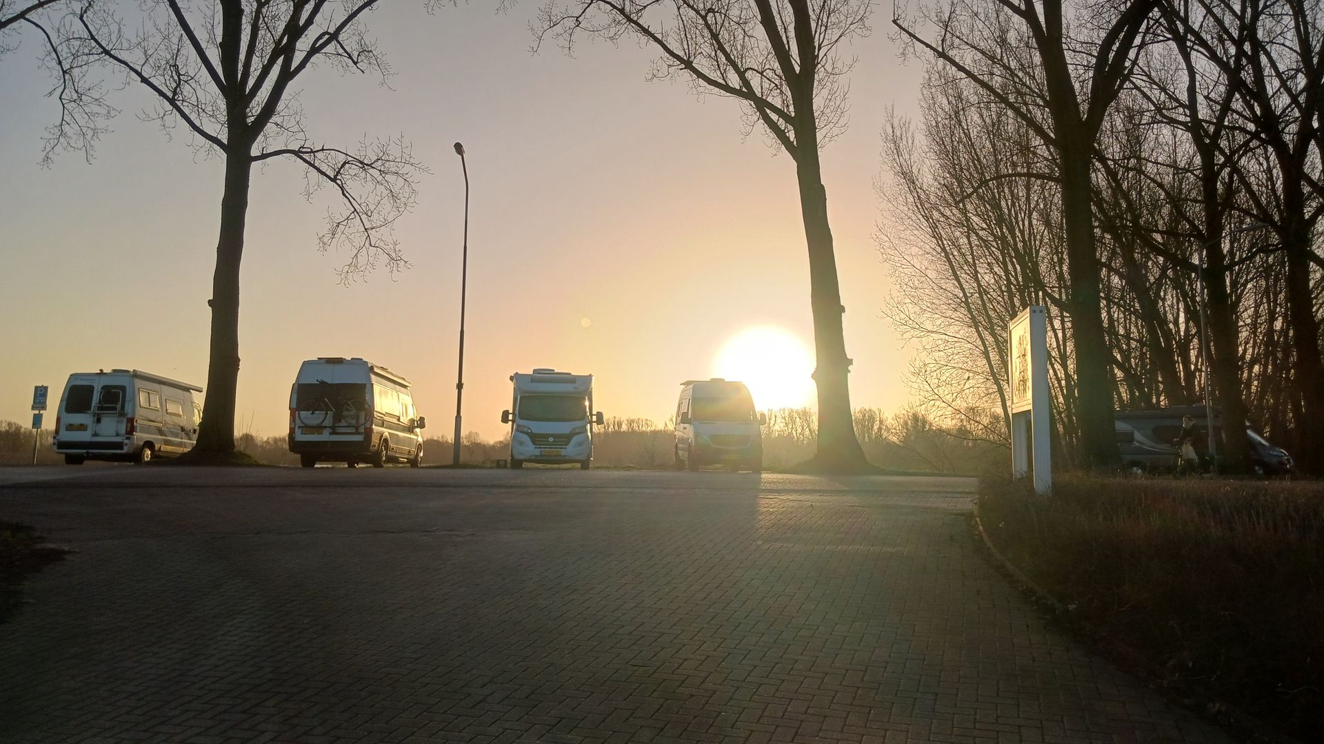 Een rij campers staat geparkeerd aan de rand van de natuur bij zonsondergang