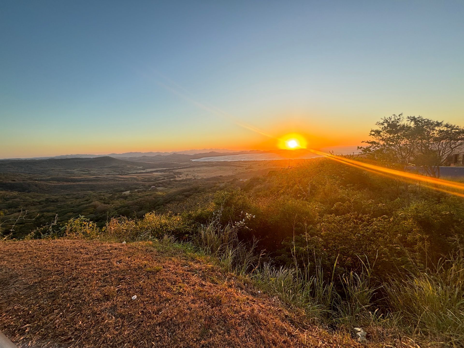 a bright orange sunrise over rolling Canadian pasturelands with a lake in the distance