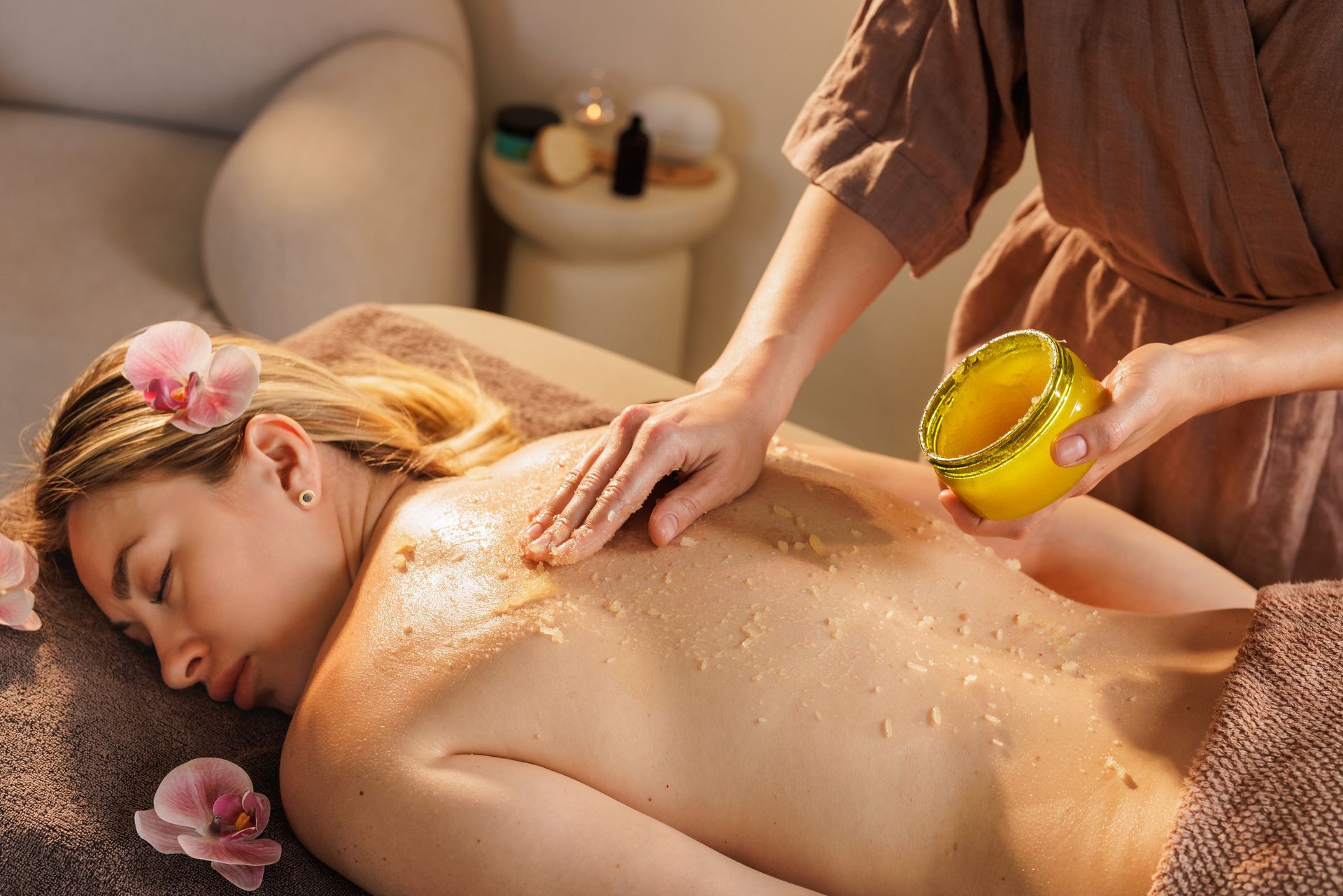 Spa massage with oils on a relaxed client lying on a table, surrounded by candles and flowers