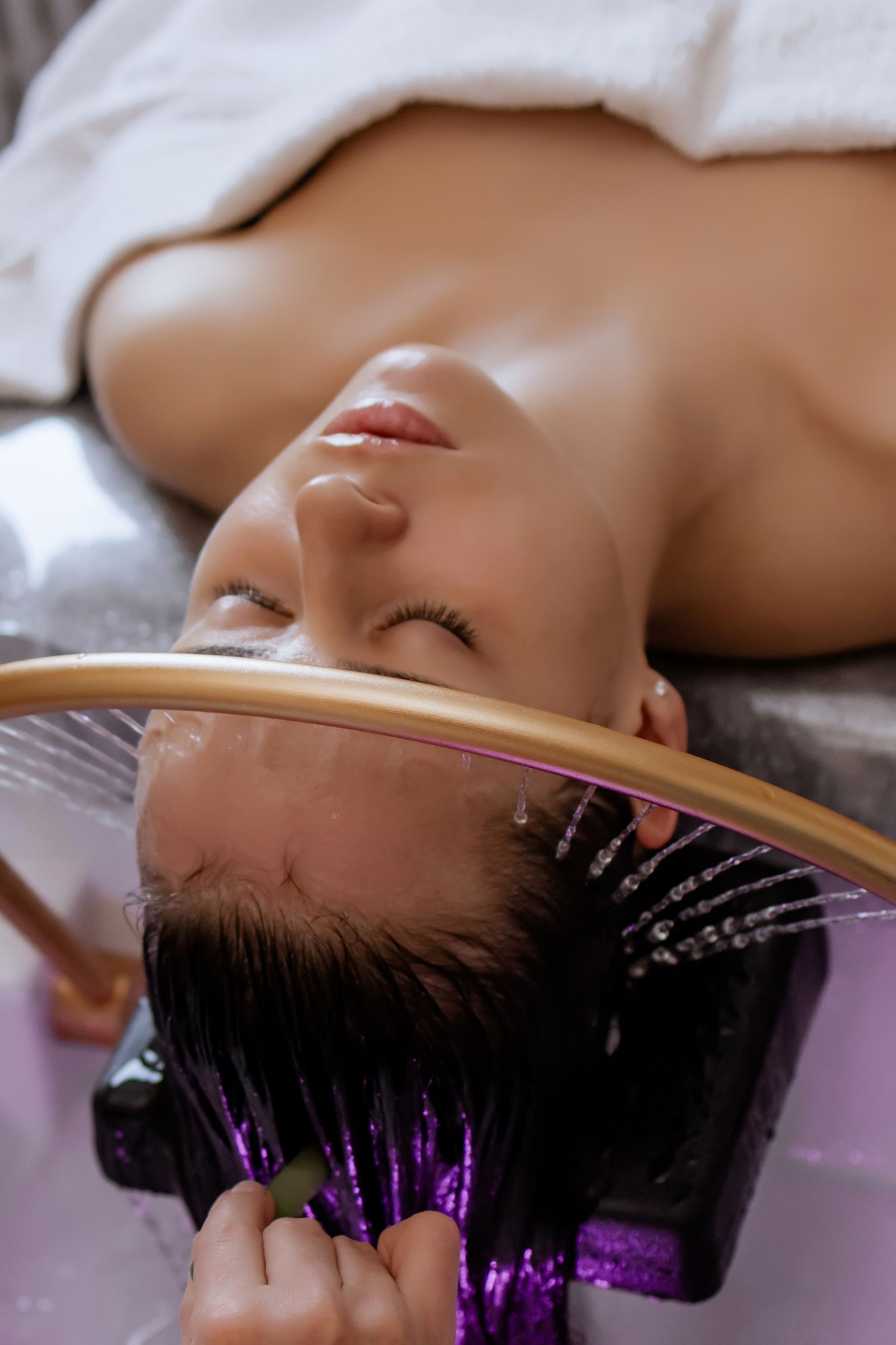 Woman receiving a shampoo at a salon wash basin, with purple-lit water rinsing her hair