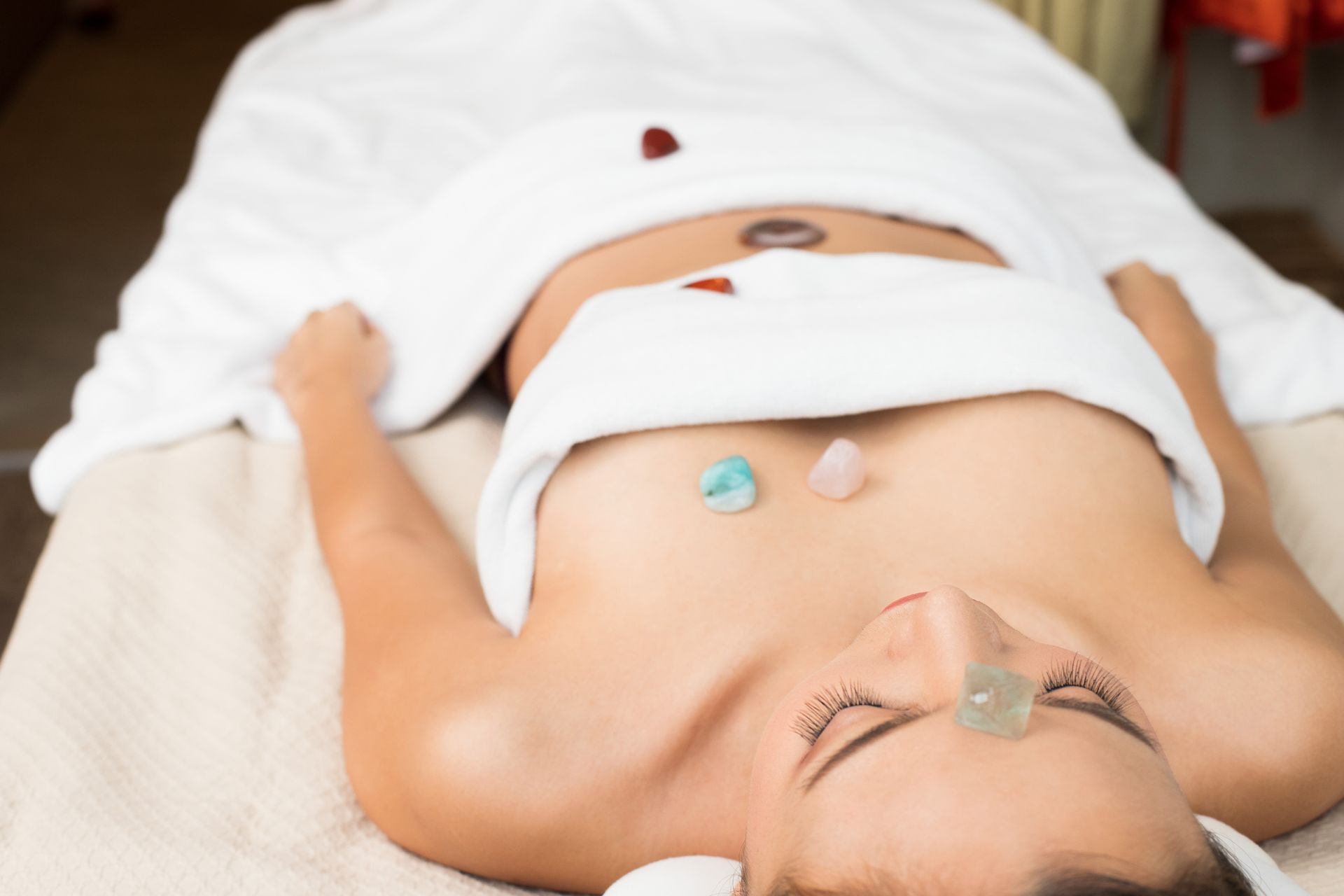 Person lying on a spa table during a facial treatment with stones on the chest and forehead