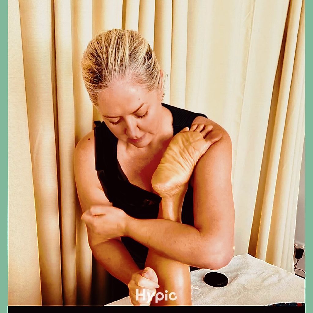 Person applying massage to shoulder and upper arm beside beige curtains