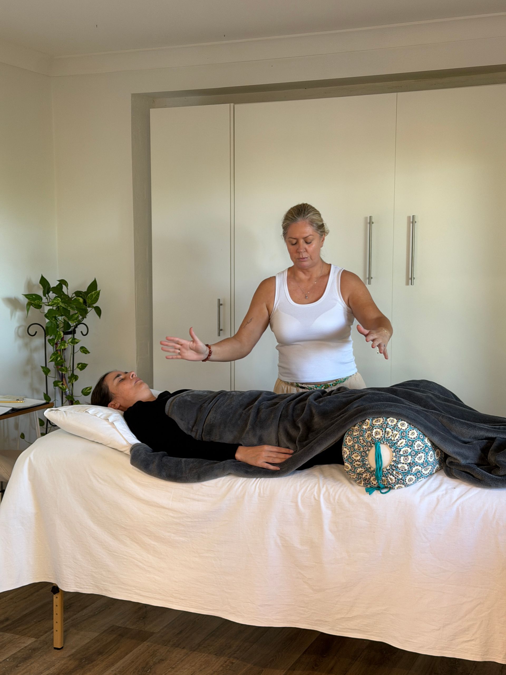 Reiki practitioner standing by a person lying on a massage table in a bright room