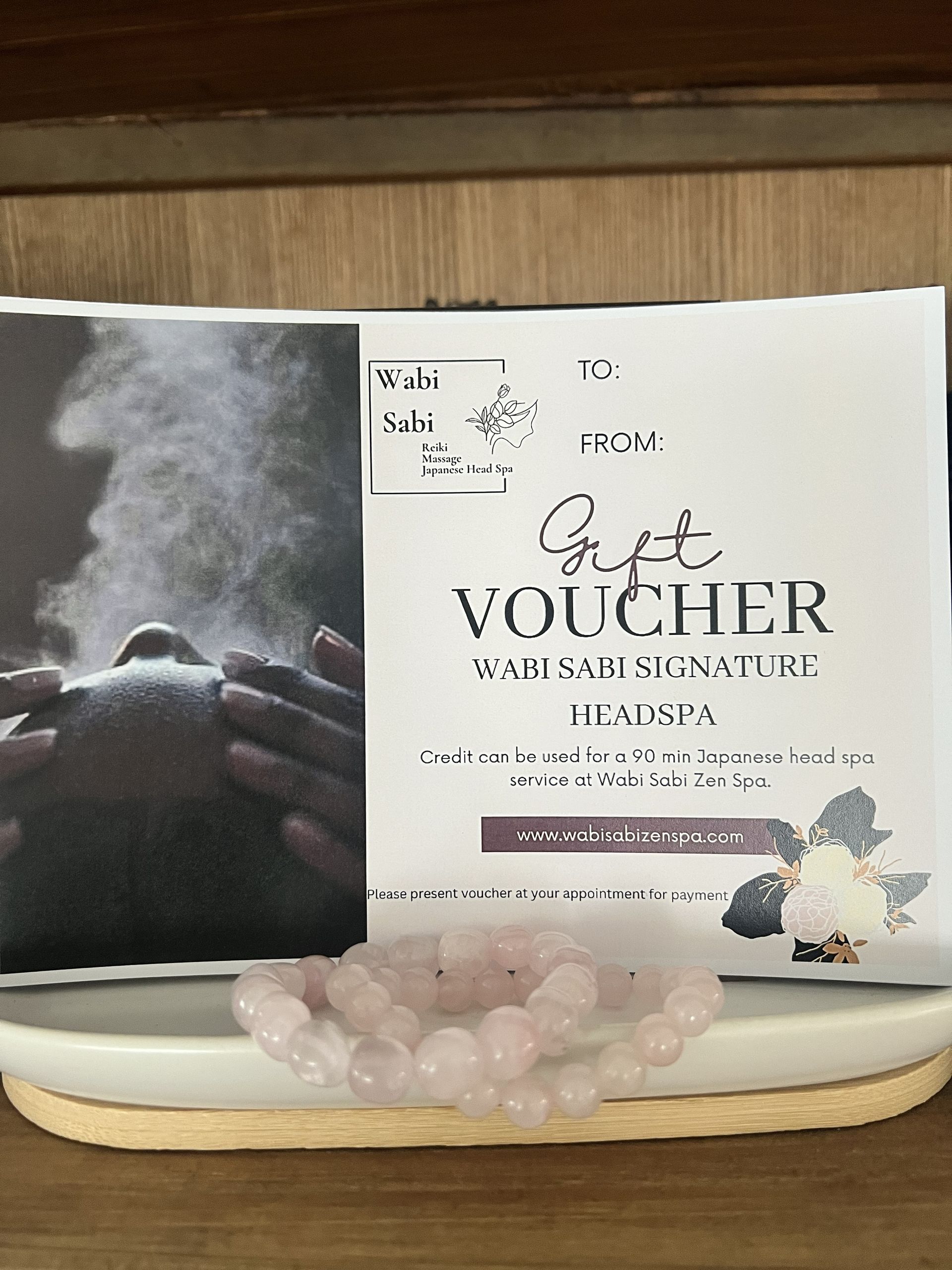 Gold voucher box with rose quartz stones and a candle on a wooden shelf