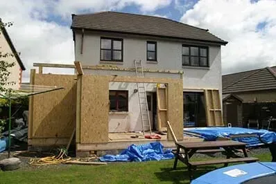 House under renovation with plywood framing, blue tarps, and a picnic table in the yard