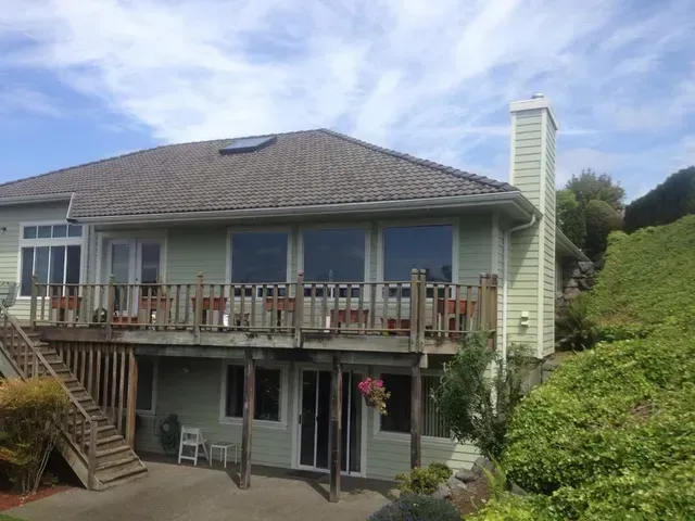 Two-story house with deck, stairs, and sliding glass doors under a blue sky