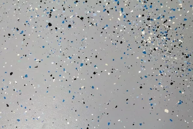 Gray speckled surface with scattered blue, black, and white flecks