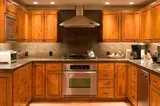 Warm-toned kitchen with wooden cabinets, stainless steel appliances, and a central stove under a range hood