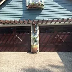 Two-car garage with maroon doors, blue siding, and a potted trellis between the doors