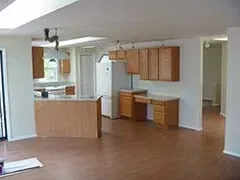 Empty open-plan kitchen and living area with wood floors, light cabinets, and a breakfast counter