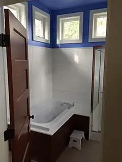 Small bathroom with blue-and-white walls, walk-in shower, window trim, and a stool.