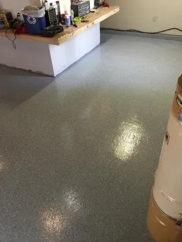 Shiny gray epoxy floor in a garage with a workbench and supplies along the wall