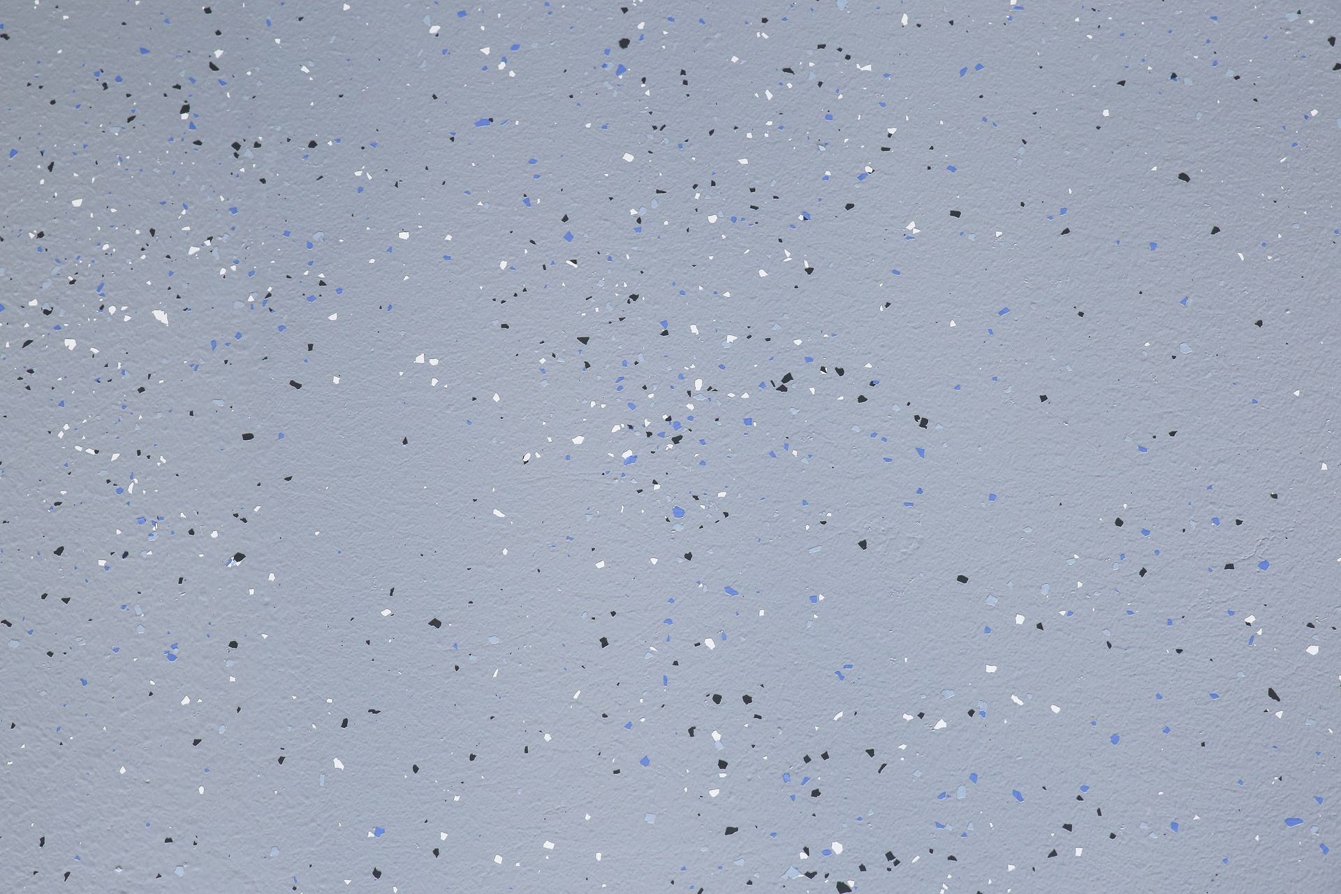 Light gray surface with scattered tiny blue and black specks, resembling textured paper or painted wall