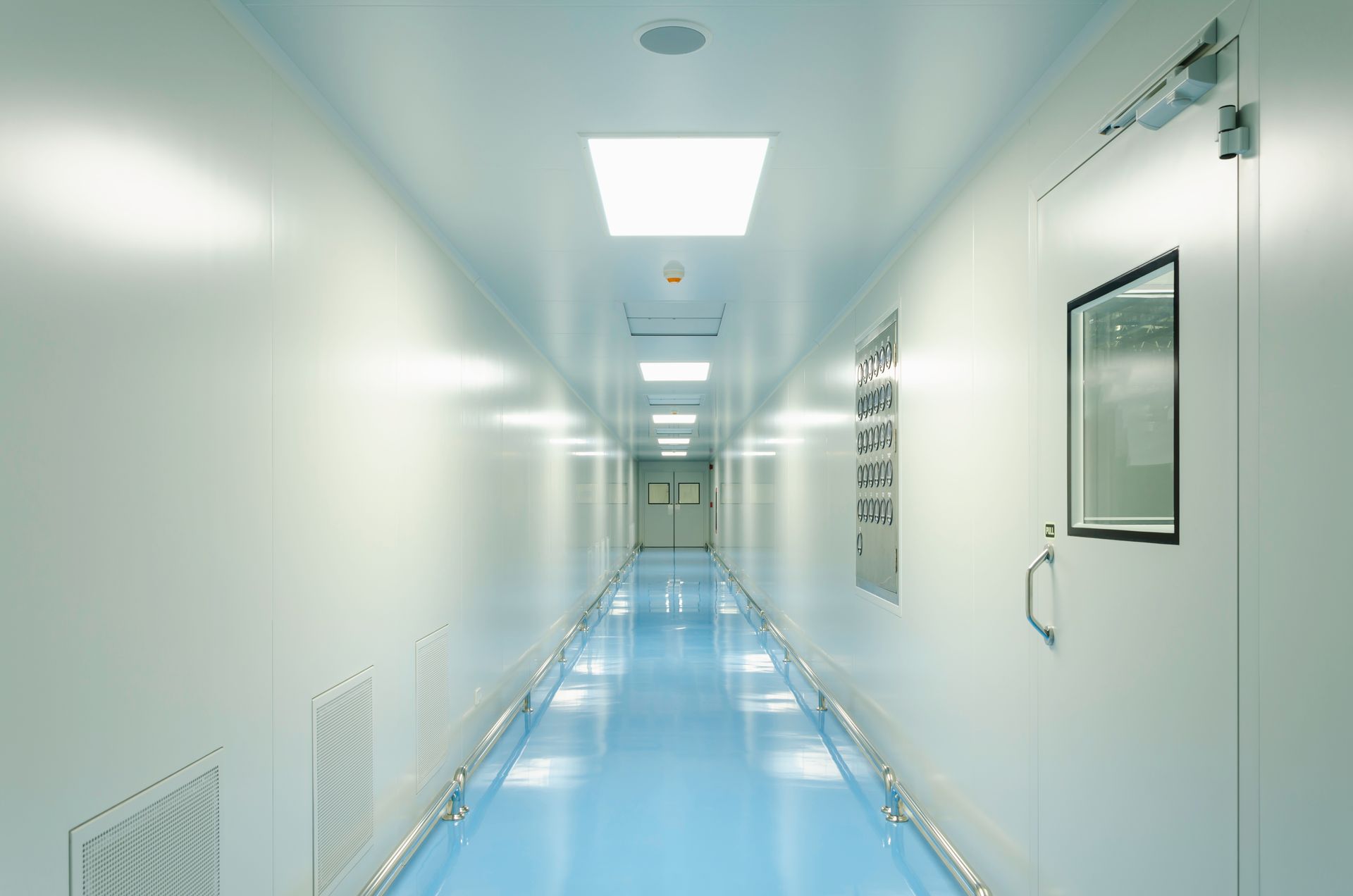 Bright white hospital corridor with blue floor and overhead lights, viewed from one end