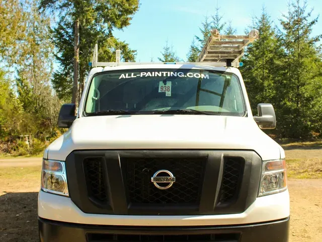 White Nissan box truck with ALL-PAINTING.COM on the windshield, parked outdoors by trees