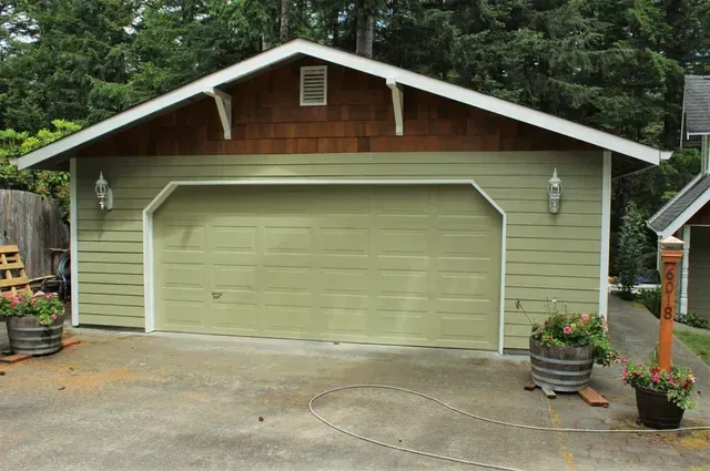 Light green garage with brown gable roof, centered on a concrete driveway, surrounded by trees.