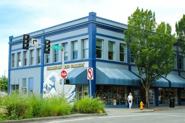 Blue corner building with awnings on a city street, trees and traffic signs outside